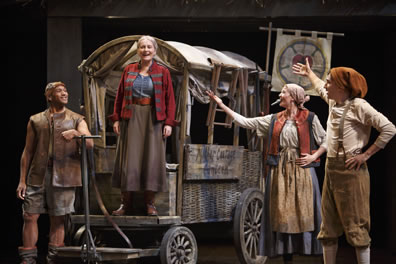 Eilif in long leather vest, cap, and shorts has his arm on the wagon yok, Mother Courage stands on the footboard of the covered wagon with its sides up, she in blue blouse, long brown dress, red coat, Kattrin with kazoo in her mouth and in peasant dress with apron, and Swiss Cheese in stocking cap, brown knee britches with suspenders over white shirt both have left hand on their hips and right spread toward Mother Courage.